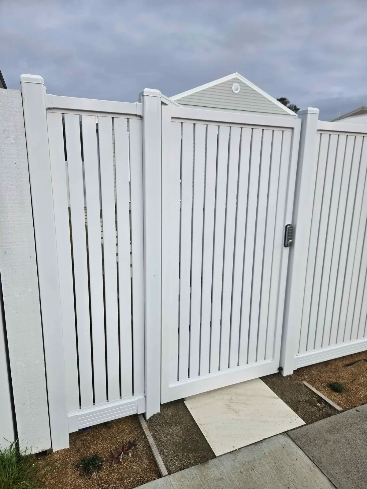 Close up of a white aluminium slat pedestrian gate with a keypad lock