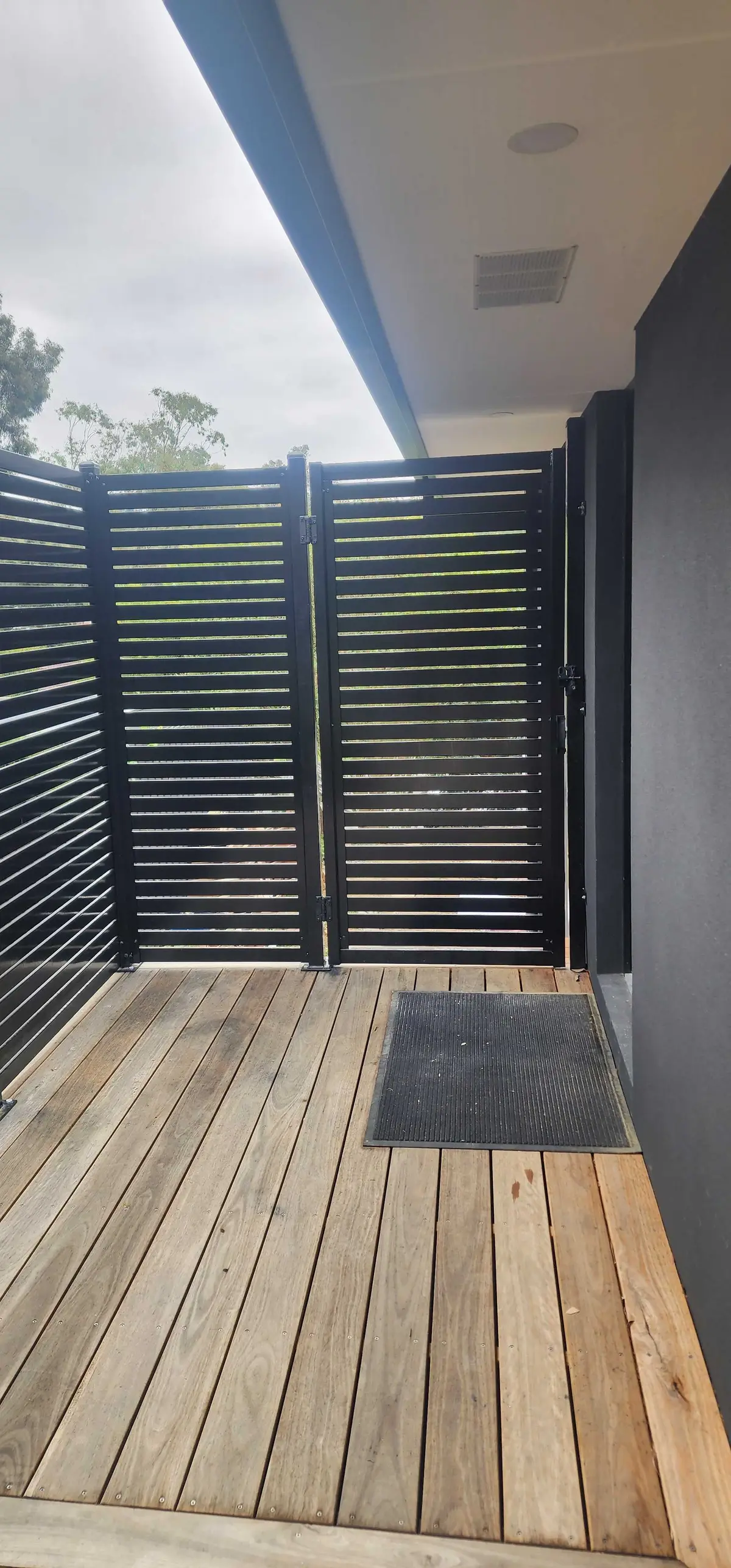 Black aluminium slat swing gate at a covered deck entry