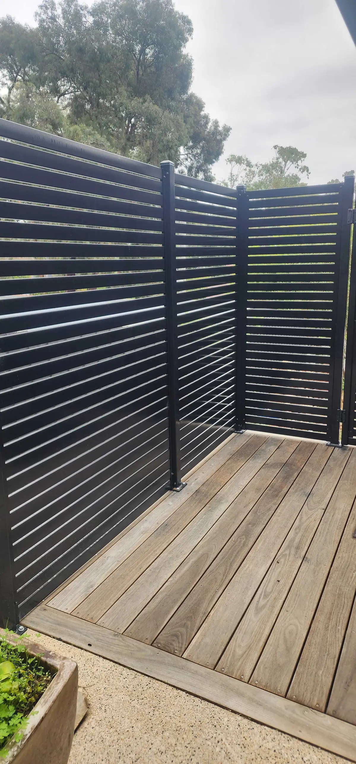 Black aluminium slat privacy screen on steel posts around a timber deck