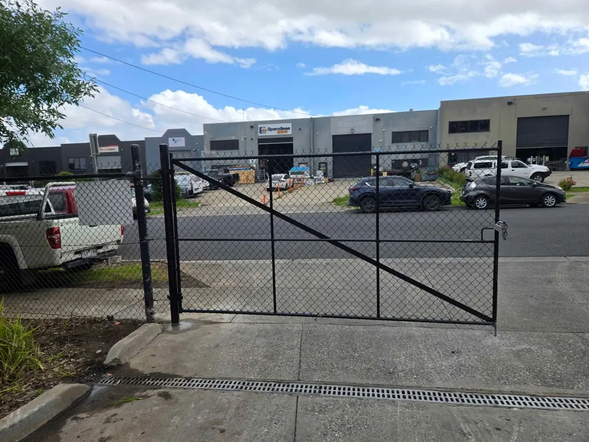 Black chain mesh swing gate across an industrial driveway with a chain and padlock, seen from inside the yard