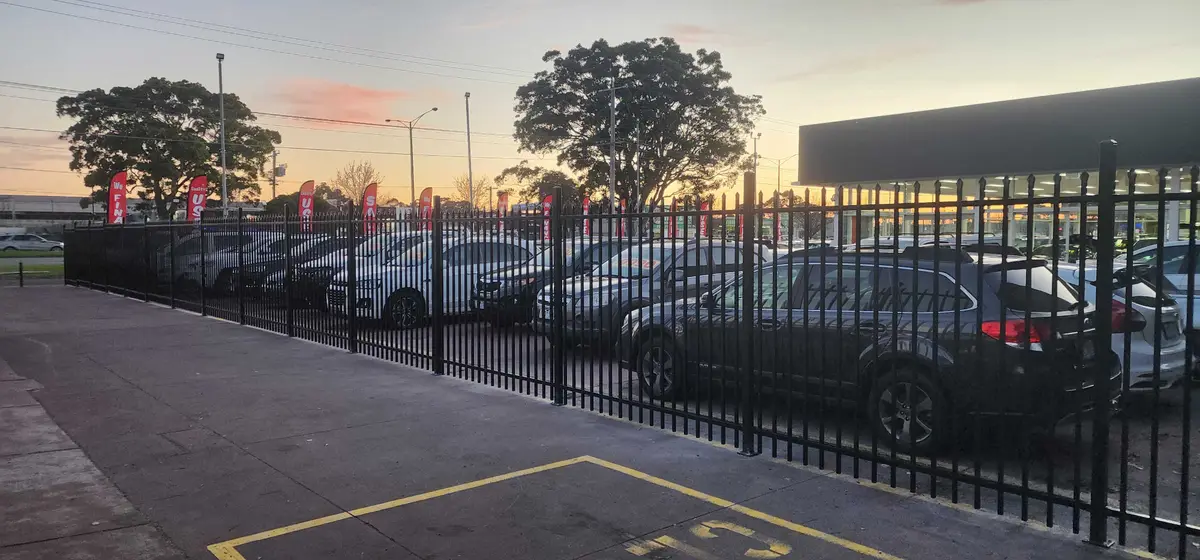 Black spear-top steel security fencing around a car dealership yard at dusk