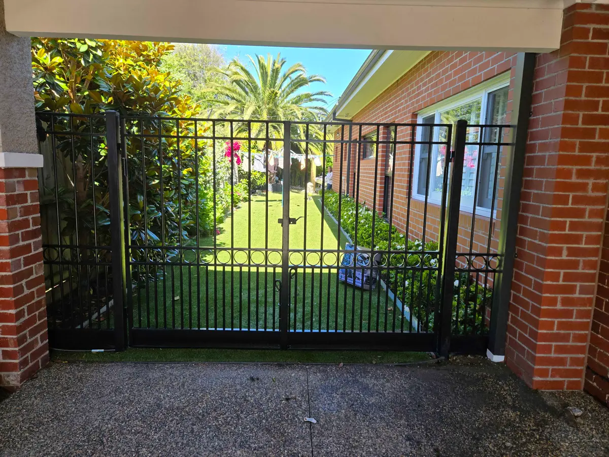 Black tubular steel double swing gates with ring detail at the side entry of a brick home