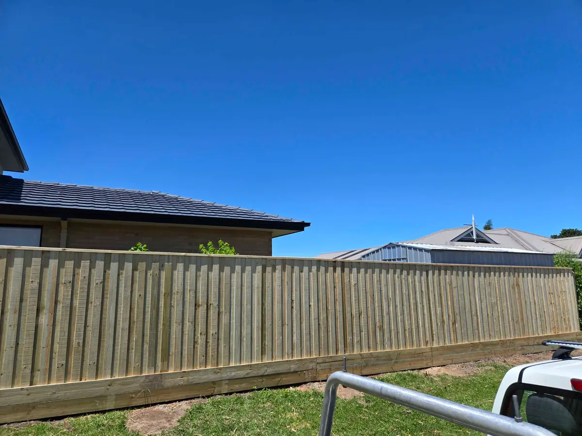 New capped treated pine paling fence beside a new brick home under a clear blue sky