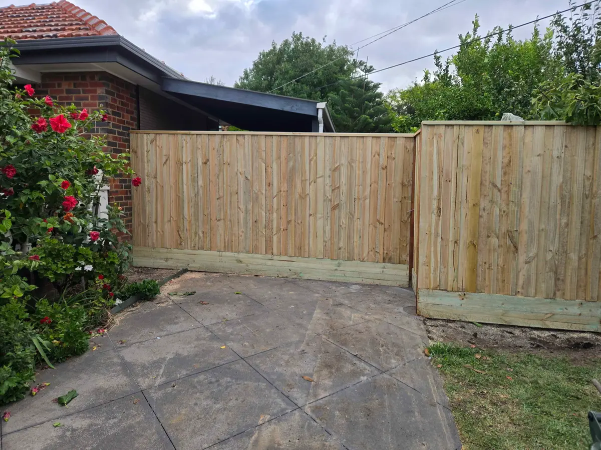 Capped timber paling fence with plinth beside a brick home and rose garden