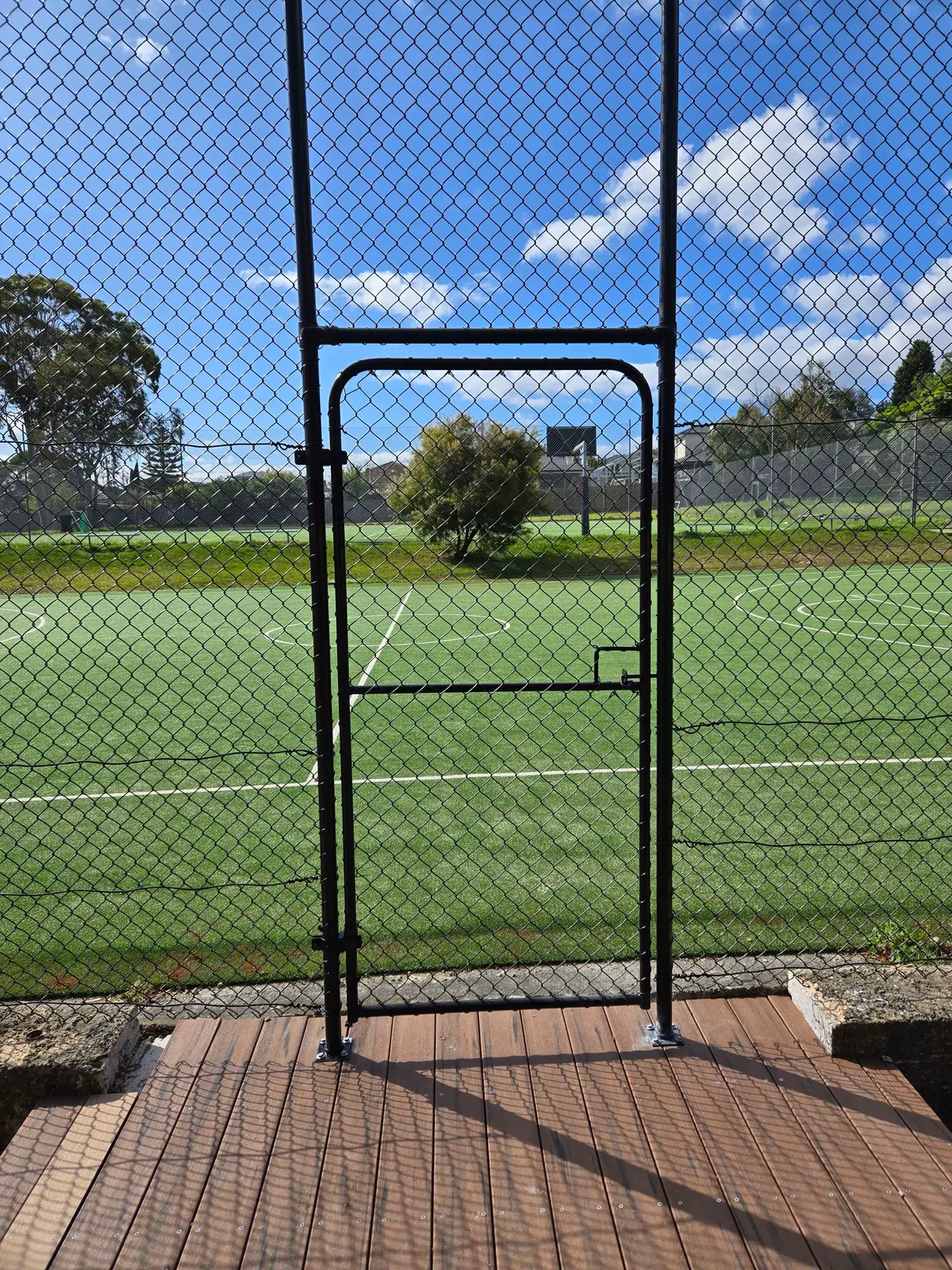Black chain mesh fence with a pedestrian gate beside a synthetic sports court