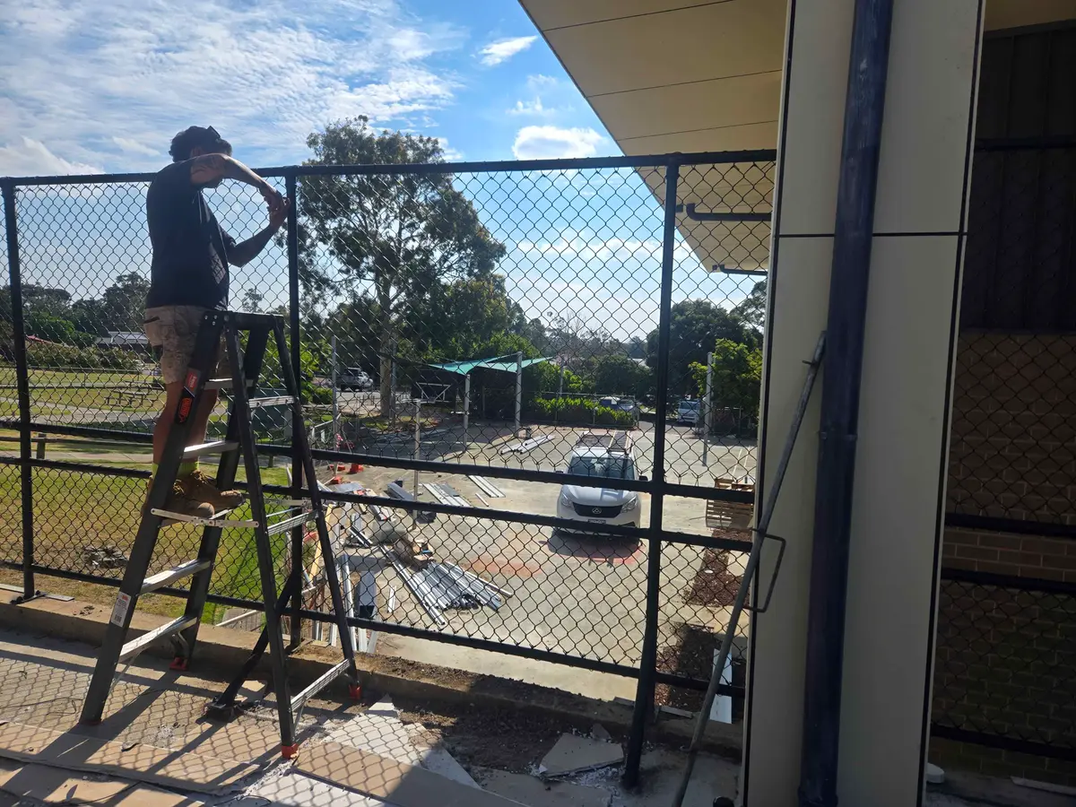 Fencer installing black chain mesh fencing on a school balcony