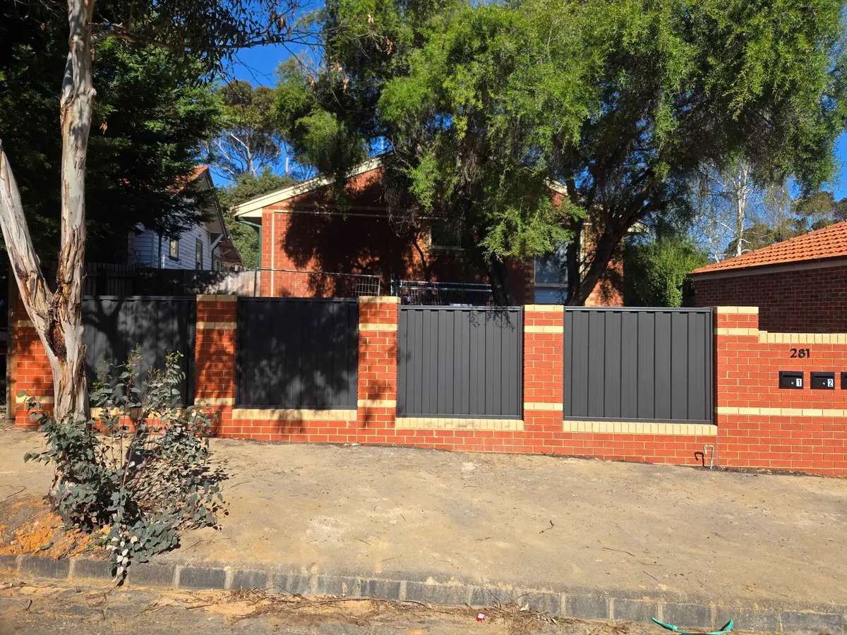 Monument Colorbond infill panels between red brick piers along the front boundary of a brick home