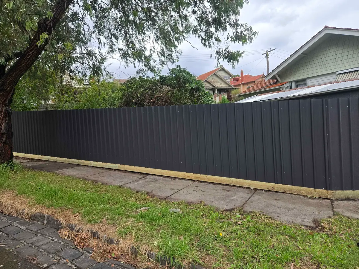 Long run of black Colorbond fence with a timber plinth along a nature strip