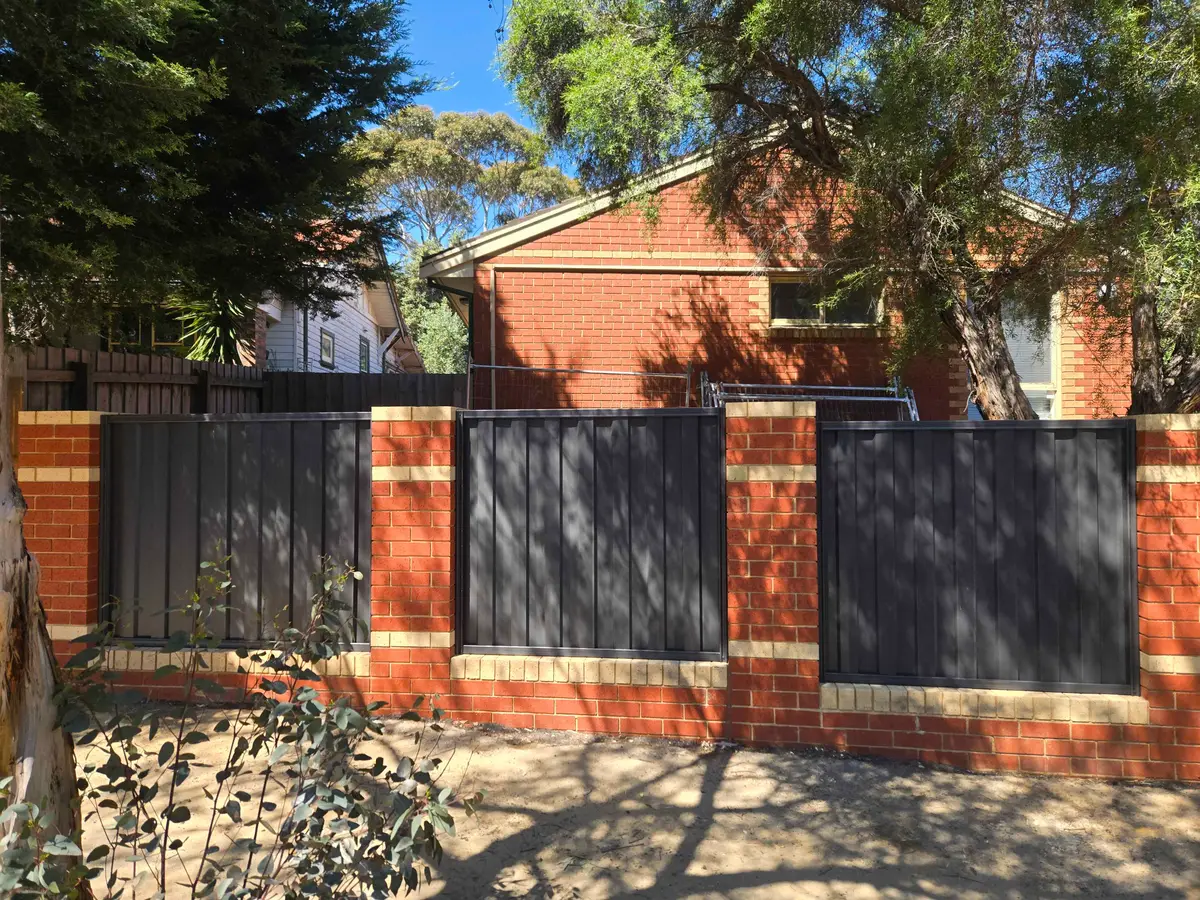 Colorbond fence panels set between brick piers on a brick plinth beside a red brick home
