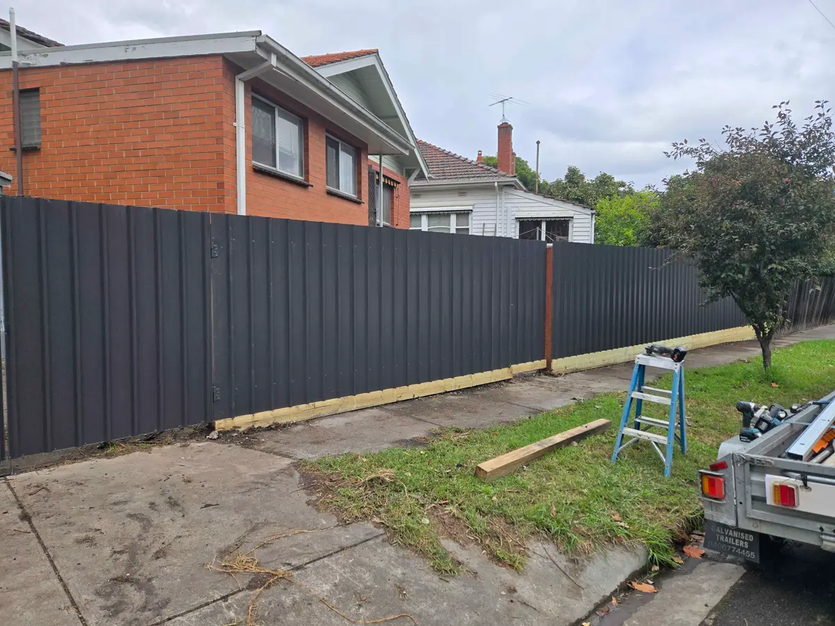 Dark grey Colorbond steel fence along a front boundary with tools and trailer on site