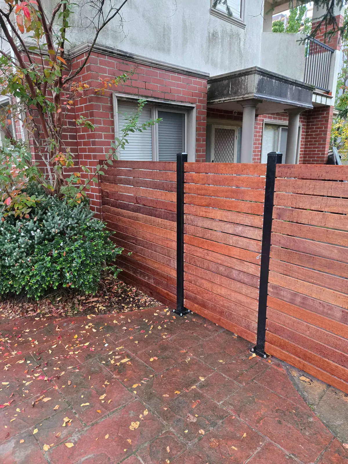 Merbau horizontal slat fence panels on black steel posts beside a garden bed
