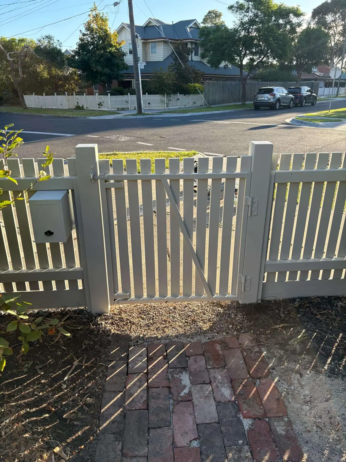 Painted timber picket fence with a braced pedestrian gate and letterbox on a corner block