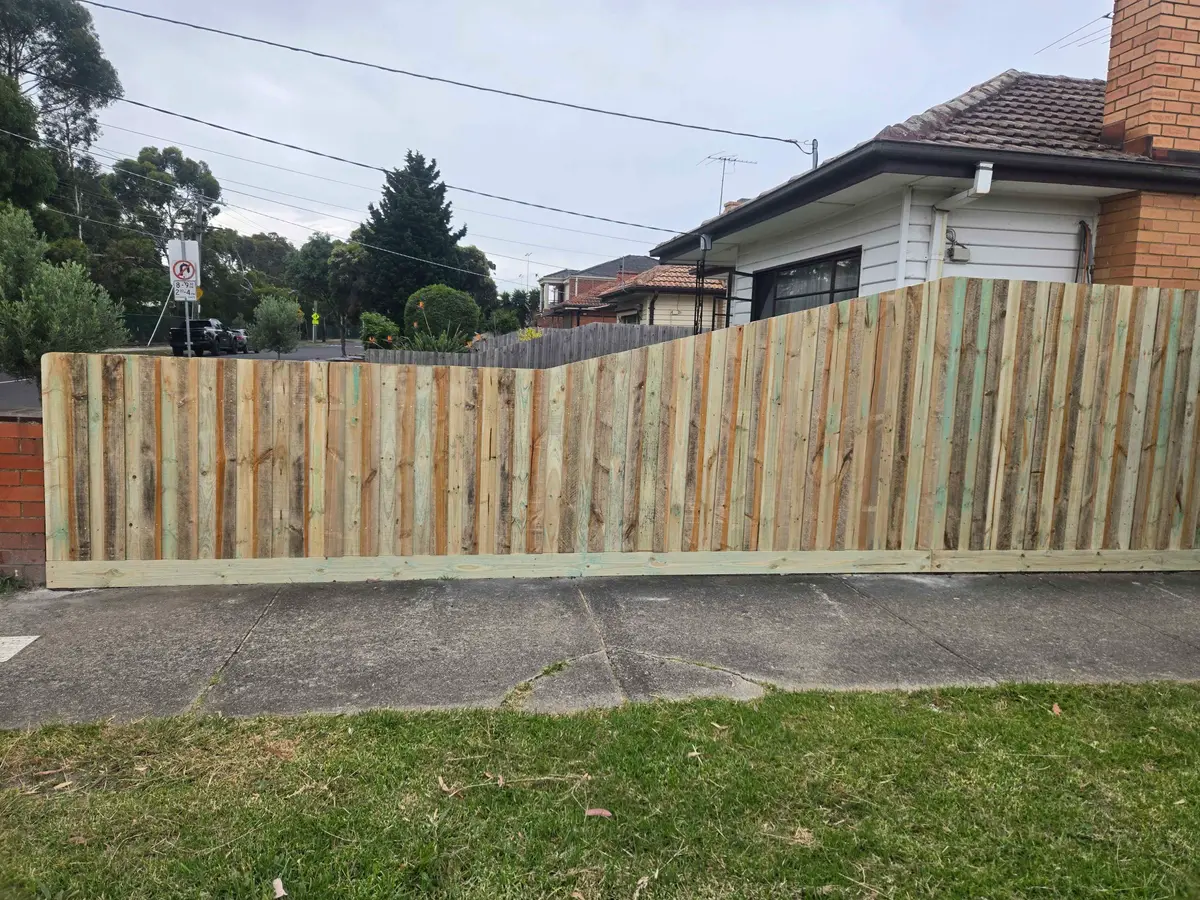 New treated pine paling fence raked down along a front boundary beside a brick pillar
