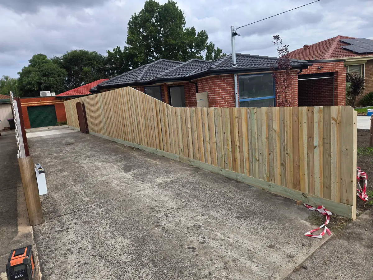 Treated pine paling fence stepping down along a driveway in front of a brick home