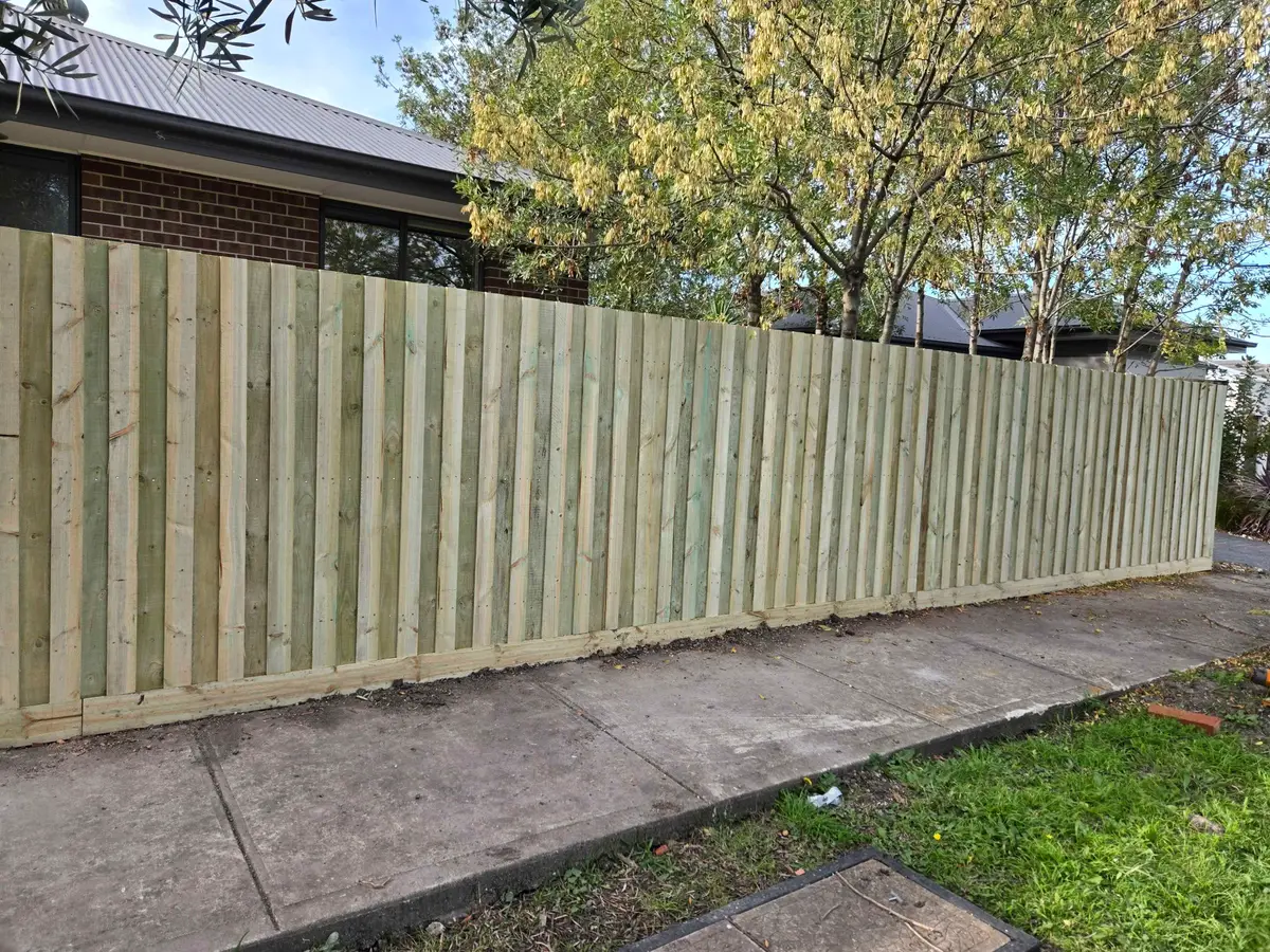 Fresh treated pine paling fence along a side boundary of a new brick home