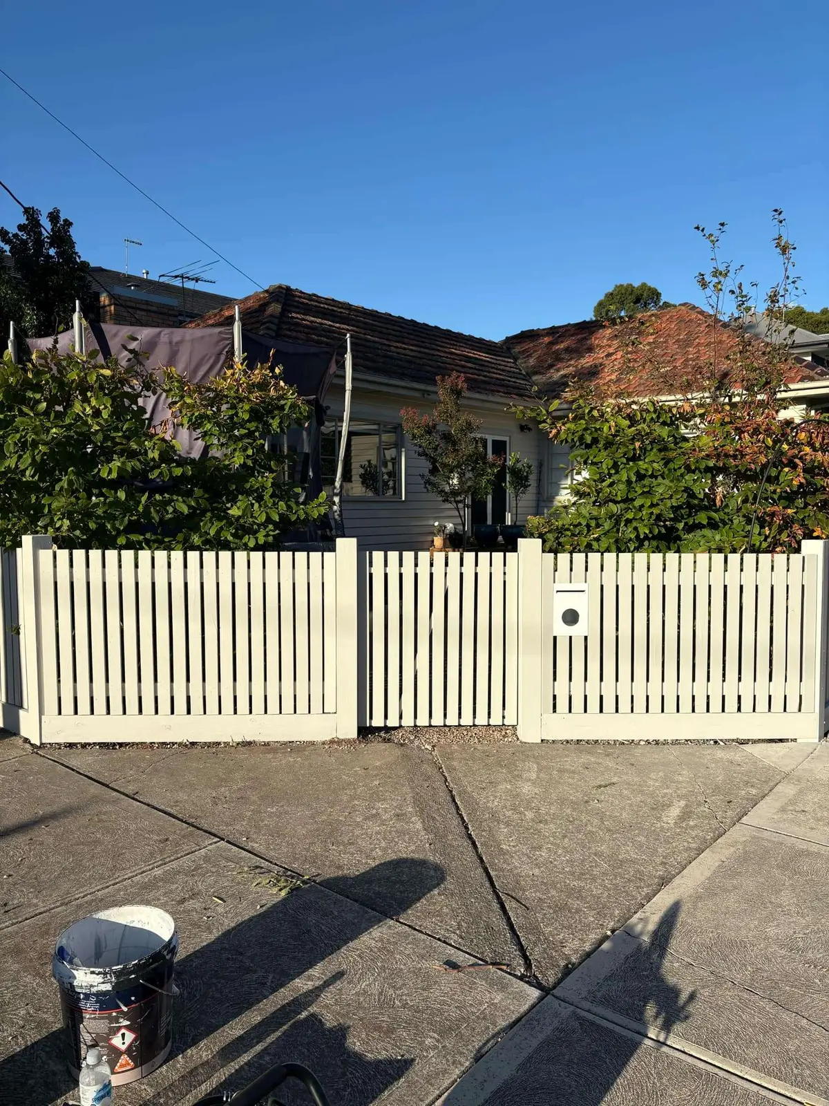 White painted picket fence with a pedestrian gate and letterbox in front of a weatherboard home