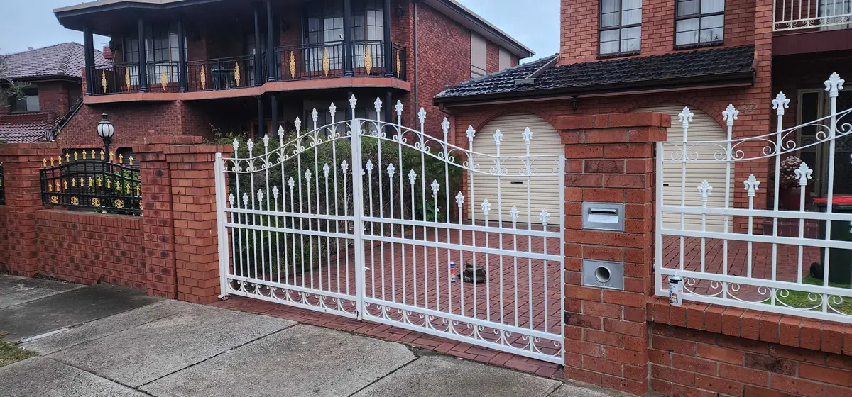 White decorative steel driveway gates and fence panels between brick pillars
